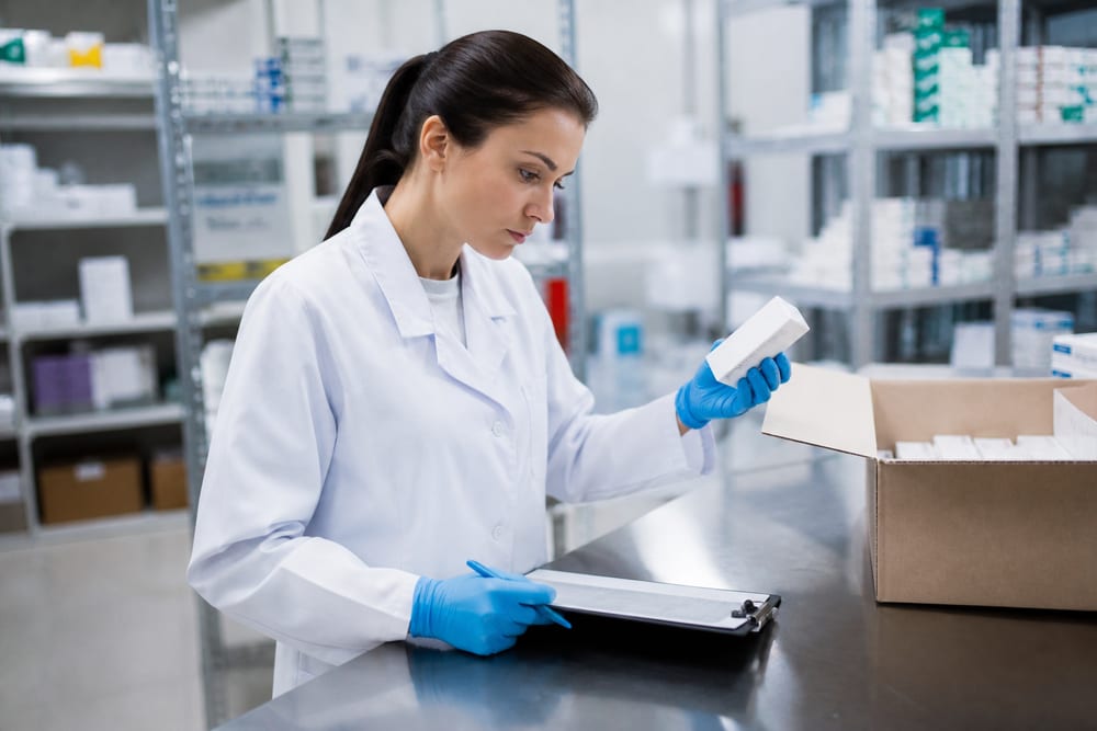 Mitarbeiterin der Qualitätssicherung prüft im Laborkittel eine Arzneimittelpackung gegen die Begleitdokumente